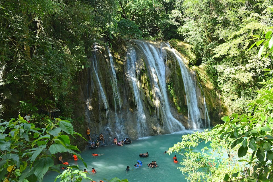 A waterfall surrounded by lush greenery and people engaging in water activities.