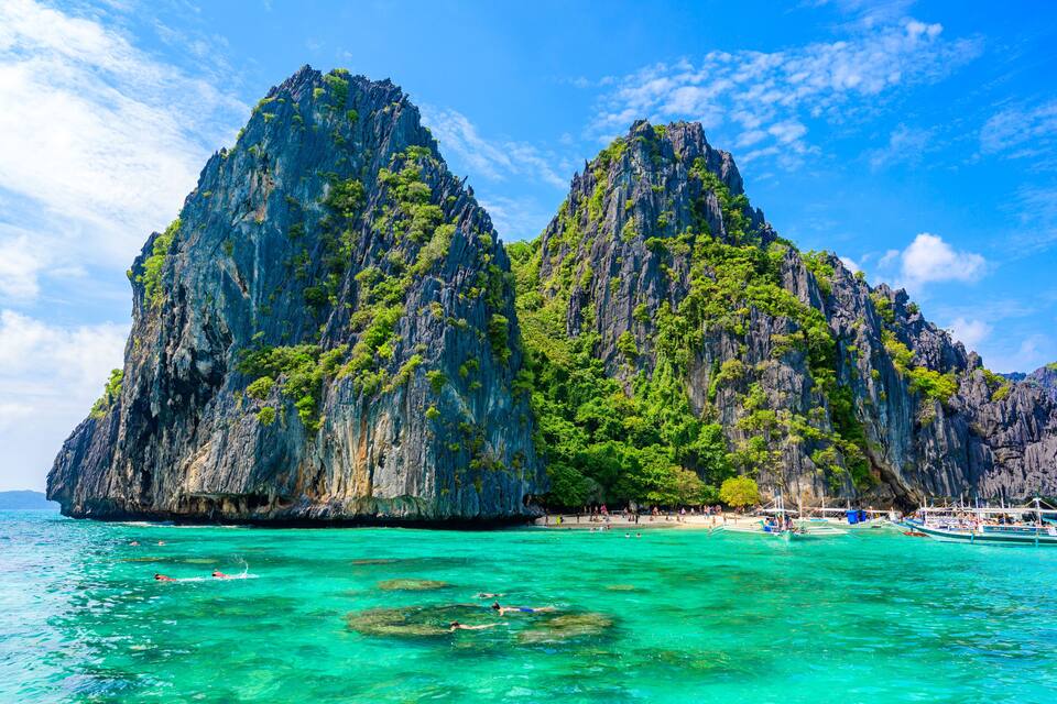 A coastal landscape with towering limestone cliffs and clear turquoise waters.