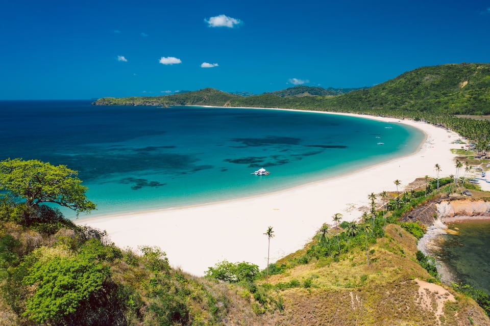 A tropical beach with clear turquoise waters, white sand, and lush greenery.