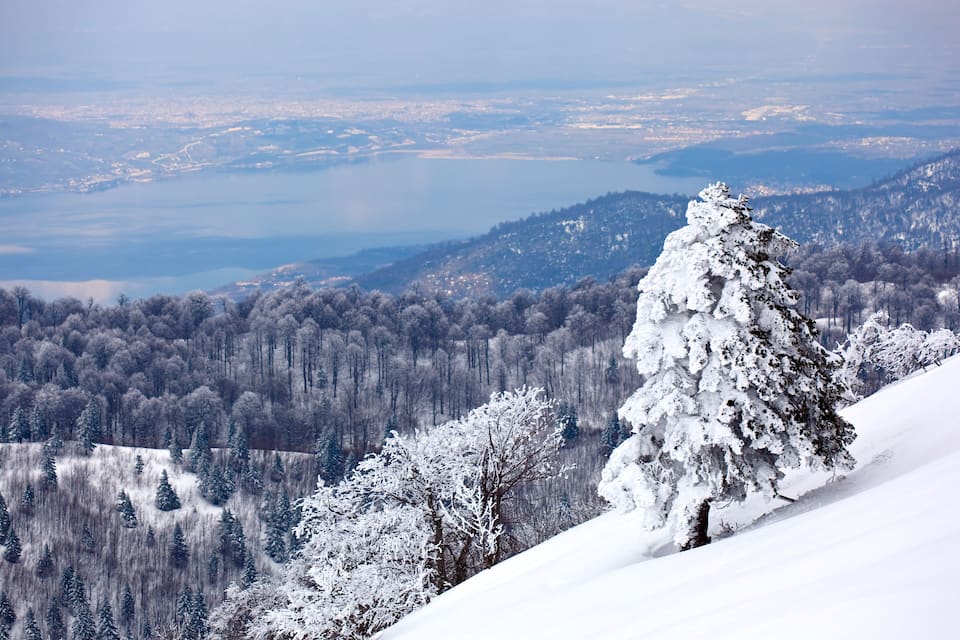 A snow-covered mountain landscape with a lake in the distance.