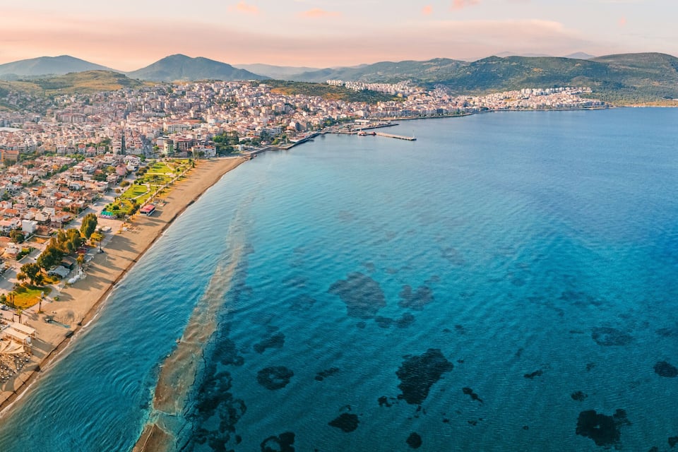 A coastal city with a beach, residential areas, and mountains in the background.