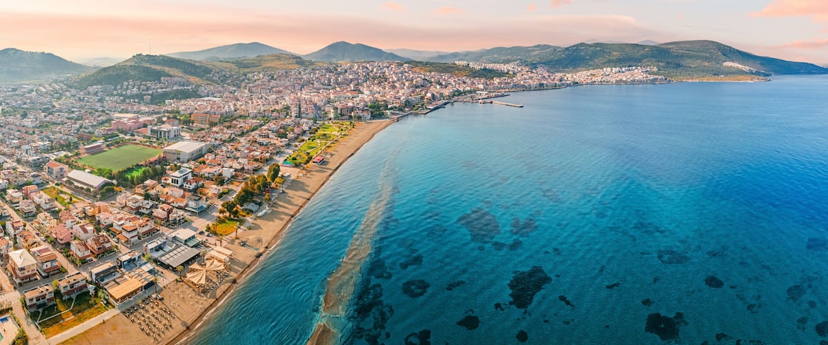 A coastal city with a beach, residential areas, and mountains in the background.