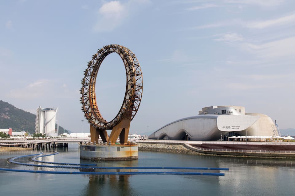 A large Ferris wheel and a modern building by the water.