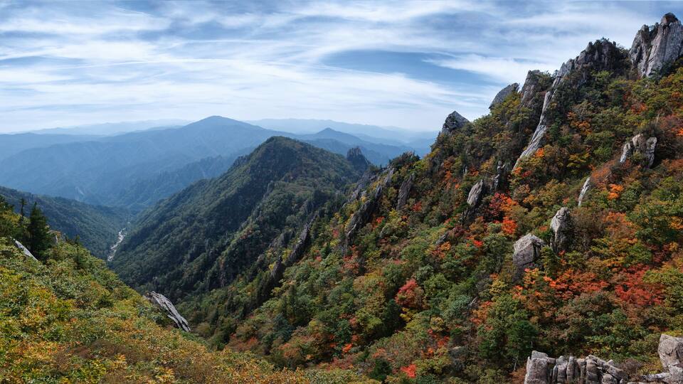 A mountainous landscape with autumn foliage, rocky outcrops, and a valley.
