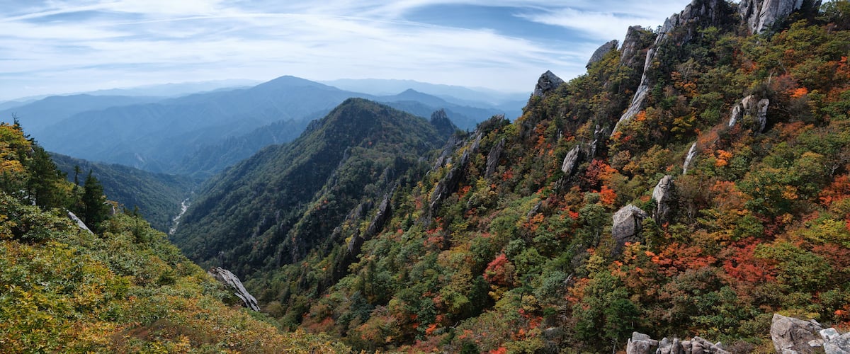 A mountainous landscape with autumn foliage, rocky outcrops, and a valley.