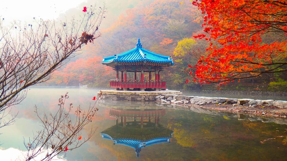 A traditional pavilion by a calm lake, surrounded by autumn foliage.
