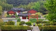 L’architecture coréenne traditionnelle se caractérise par des bâtiments rouges et des toits couverts de tuiles grises, le tout étant entouré d’une végétation luxuriante et d’arbres.