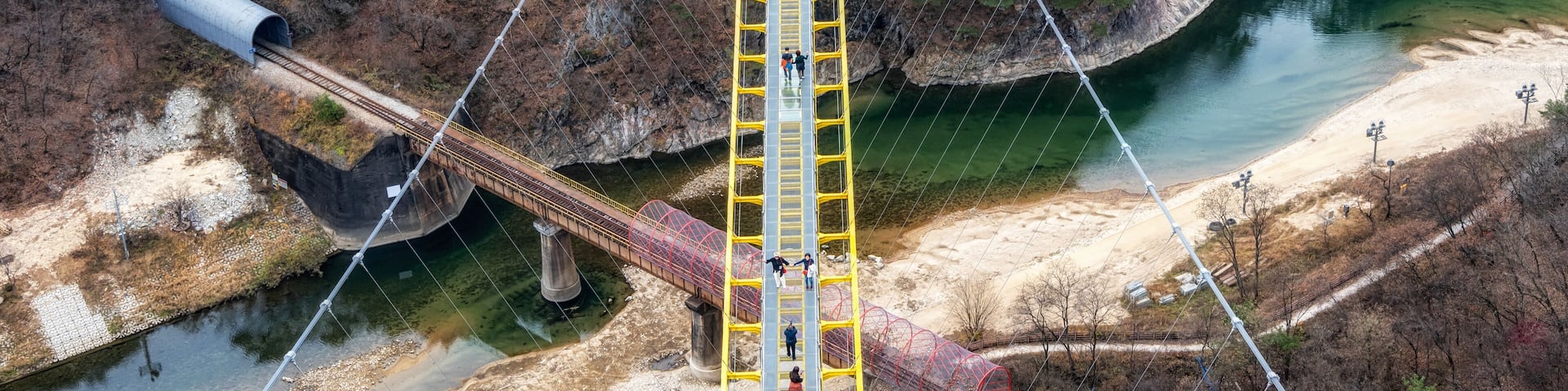 A suspension bridge over a river with a rocky cliffside and sparse vegetation.