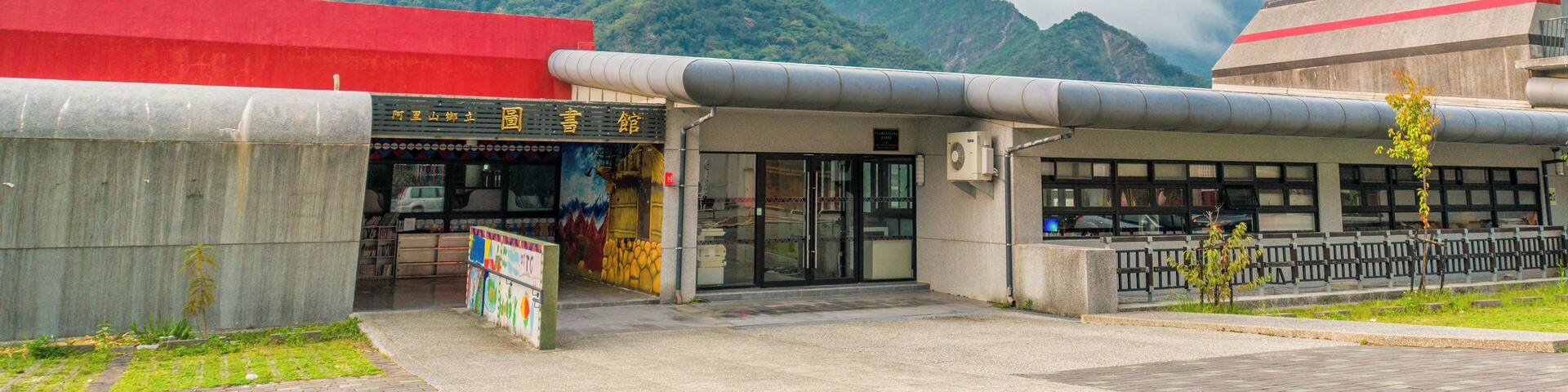 A building with a red roof and a sign with Chinese characters. There is a mountain in the background and a tall communication tower to the left.
