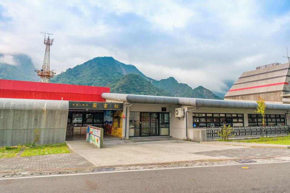 A building with a red roof and a sign with Chinese characters. There is a mountain in the background and a tall communication tower to the left.