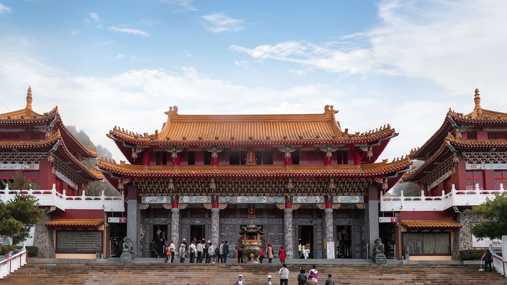 Ein traditionelles chinesisches Gebäude mit aufwendigen roten und goldenen Dächern, mehreren Ebenen und einer breiten Treppe, die zum Eingang führt.