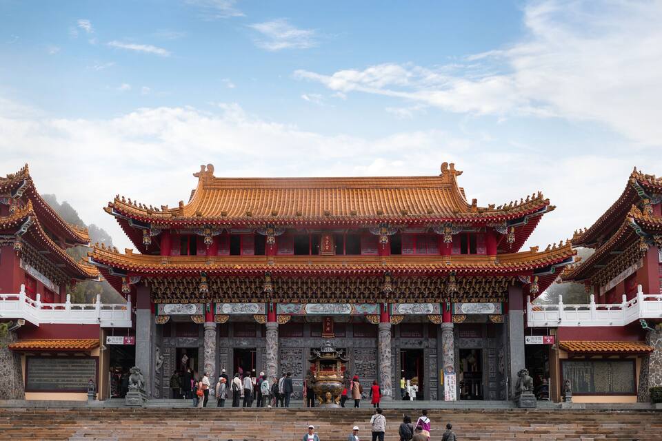 Um edifício tradicional chinês com telhados elaborados em vermelho e dourado, vários níveis e uma grande escadaria que leva à entrada.