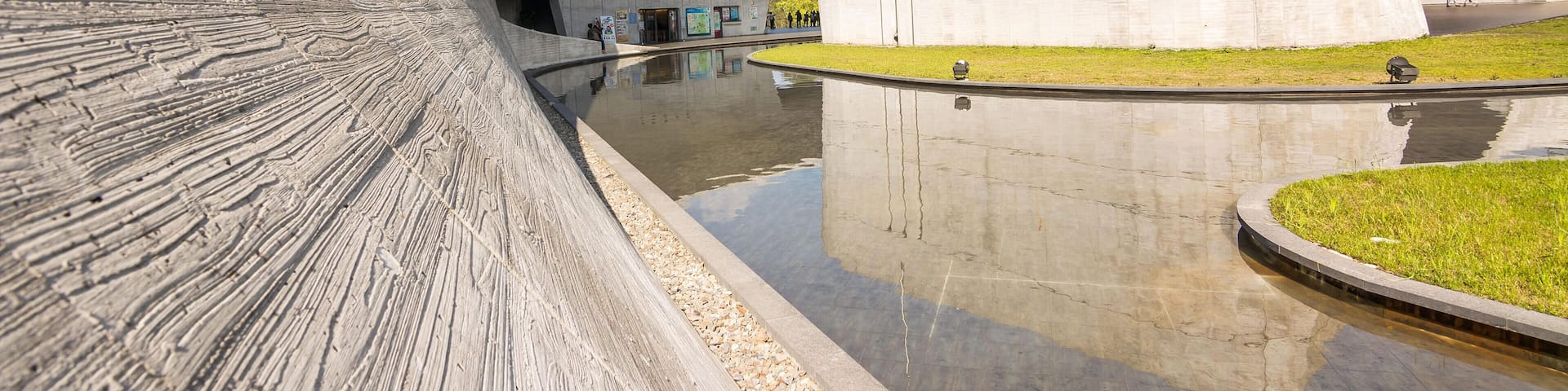 A modern architectural structure with a curved facade and a reflective water feature.