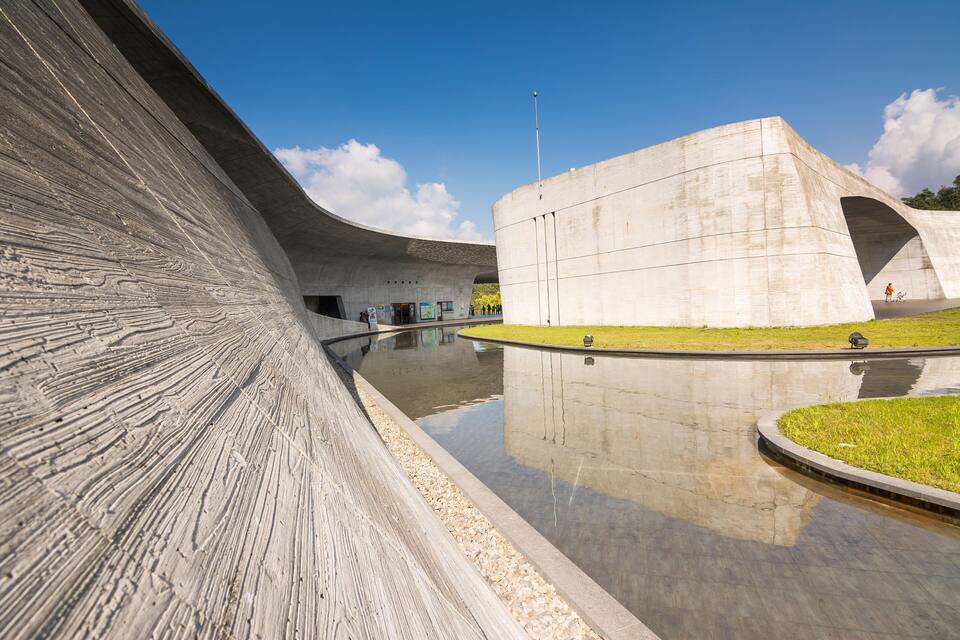 Uma estrutura arquitetônica moderna com fachada curva e um espelho d'água refletivo.