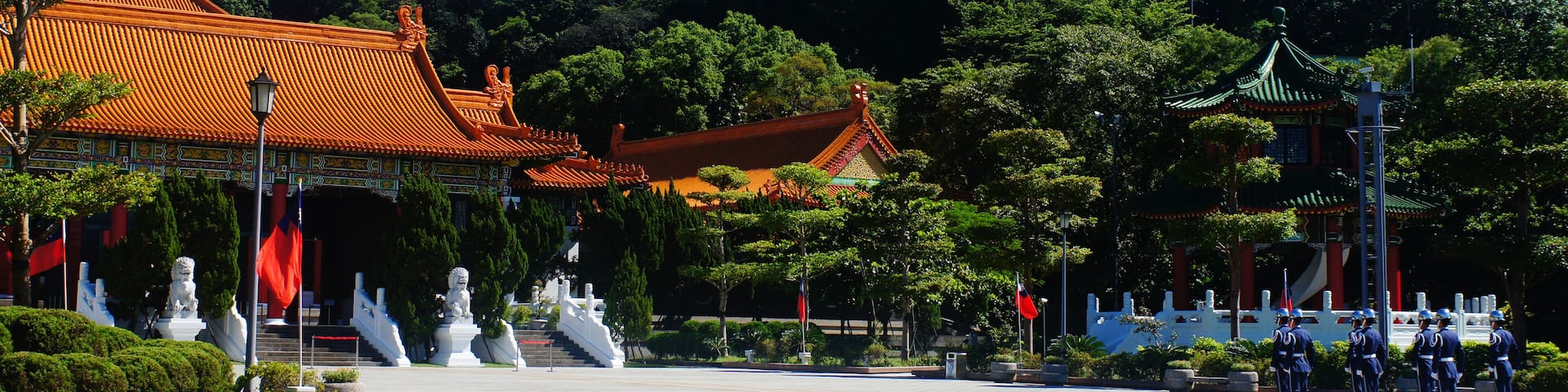 A traditional Chinese building with a red roof, surrounded by lush greenery and statues.