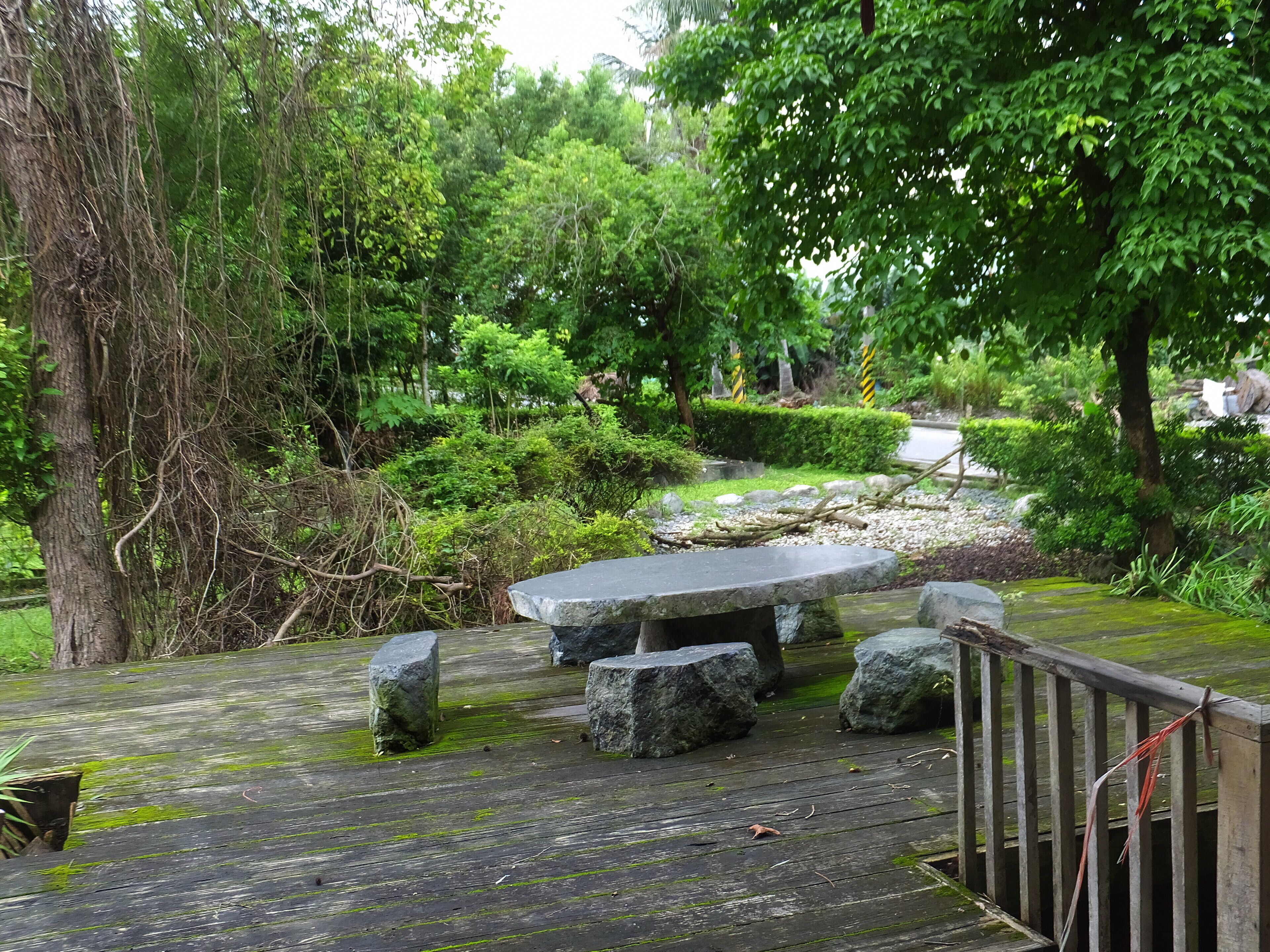 A wooden deck with a stone bench surrounded by lush greenery and trees.