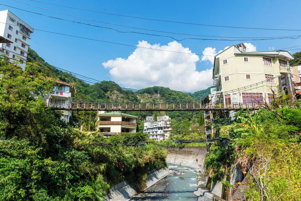 A bridge over a river, surrounded by lush greenery and buildings.