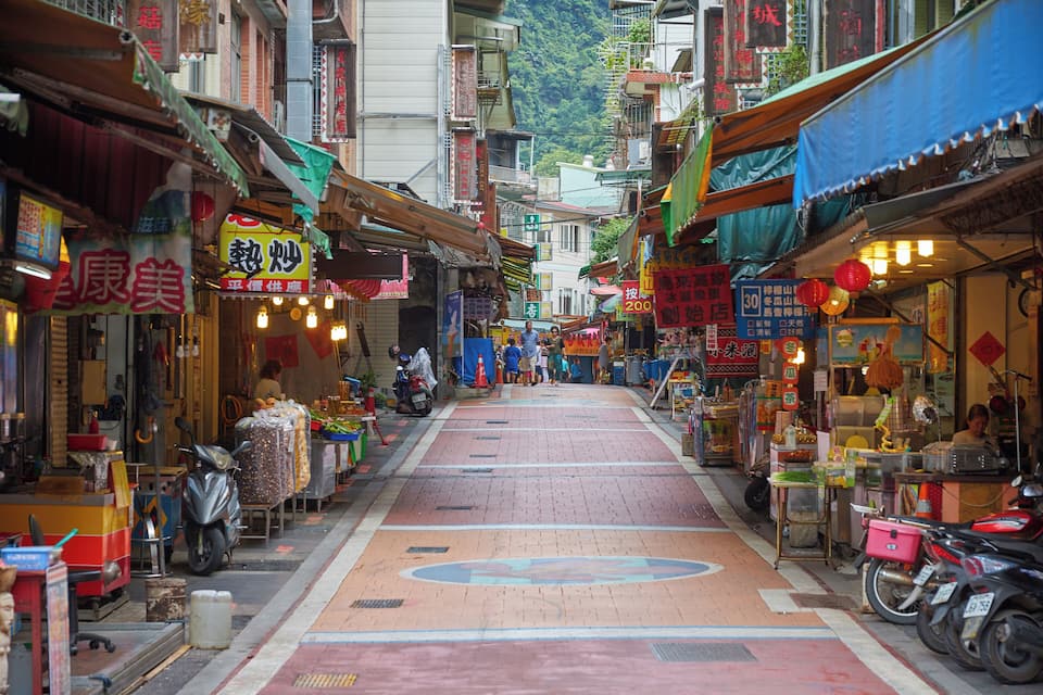 A narrow street lined with shops and motorcycles.