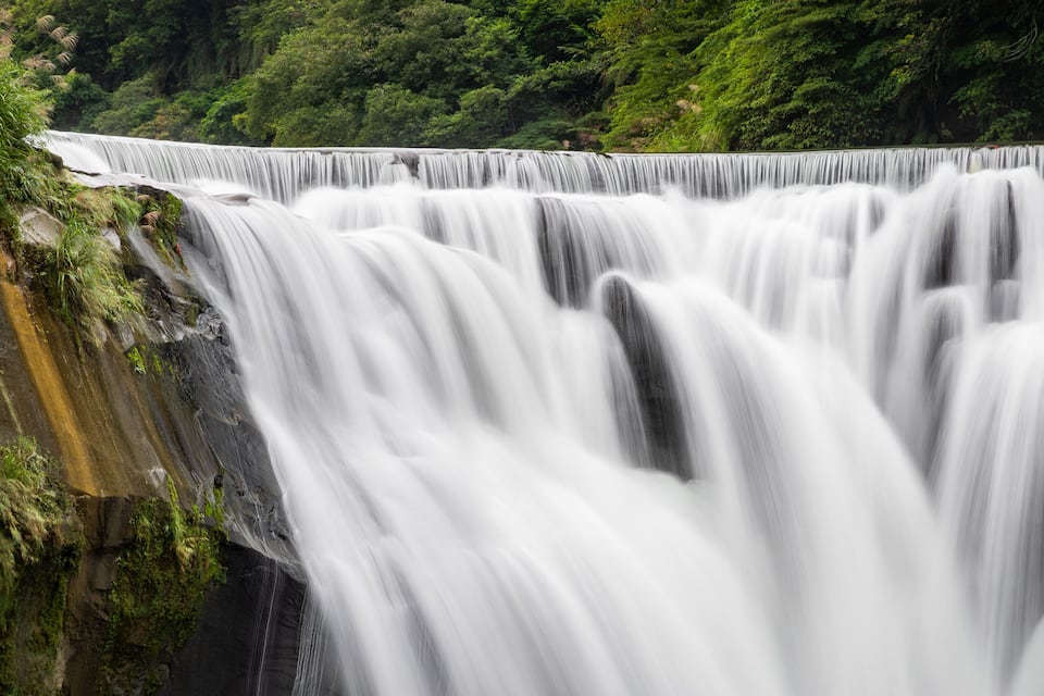 A multi-tiered waterfall surrounded by lush greenery.