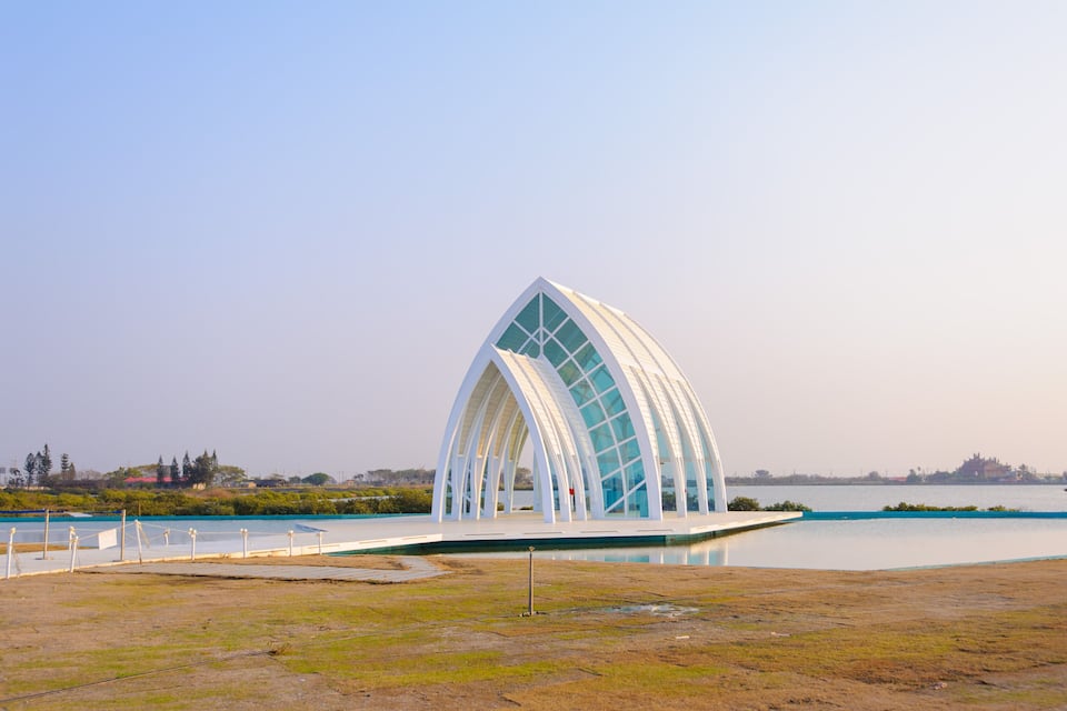 Um edifício moderno e branco, com um telhado arqueado singular, próximo a um corpo de água.