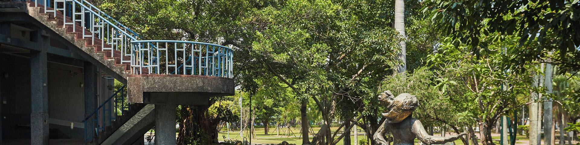 Un parc avec un étang, une statue et un escalier menant à un bâtiment.