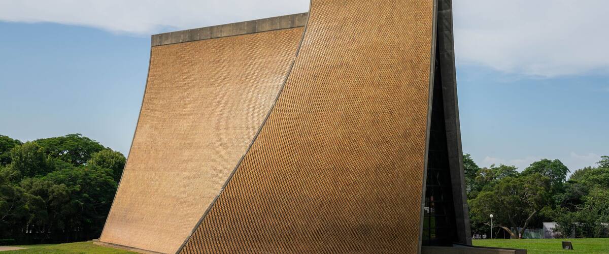 The Luce Memorial Chapel at Tunghai University stands majestically against the backdrop of a clear blue sky, its striking modern architecture beautifully complemented by the lush greenery surrounding