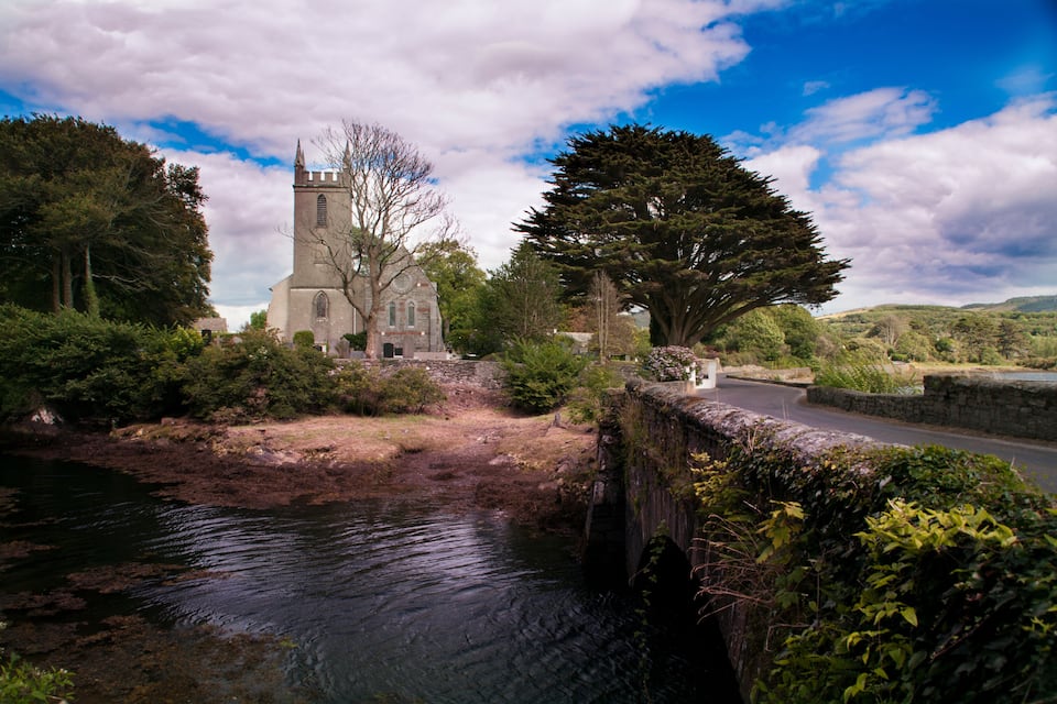 A stone bridge over a river, a church with a tower, and surrounding greenery.