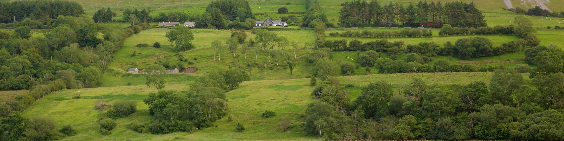 A mountainous landscape with a lake in the foreground and a house on a hill.