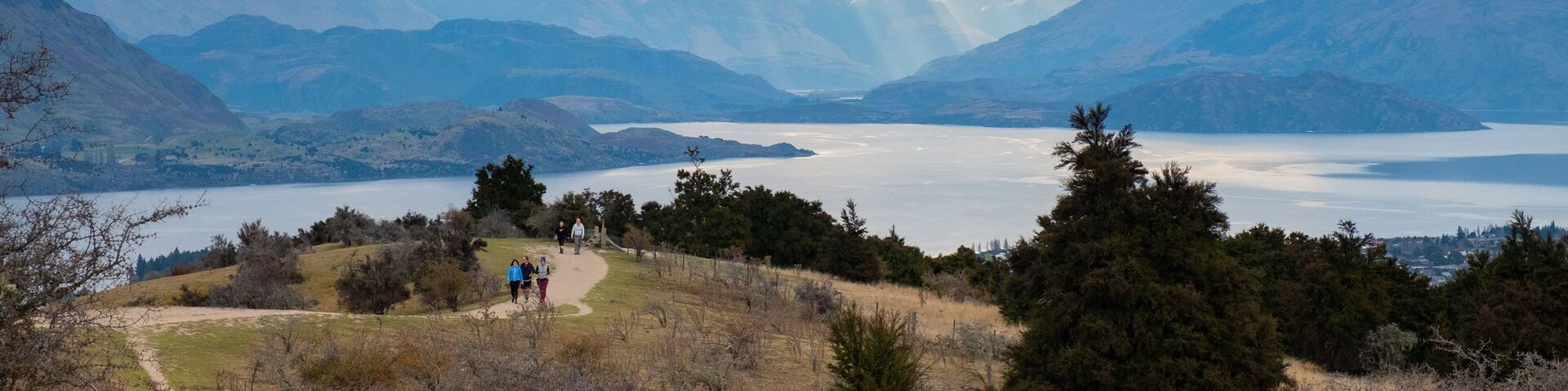 A mountainous landscape with a lake and a path with people walking.