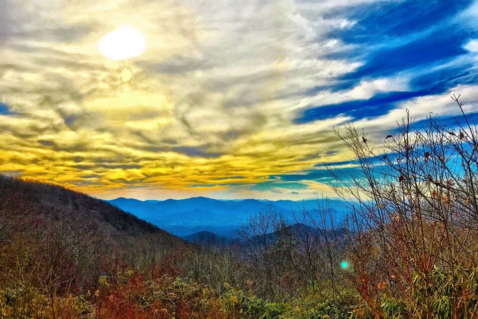 A mountainous landscape with autumn foliage and a dramatic sunset sky.