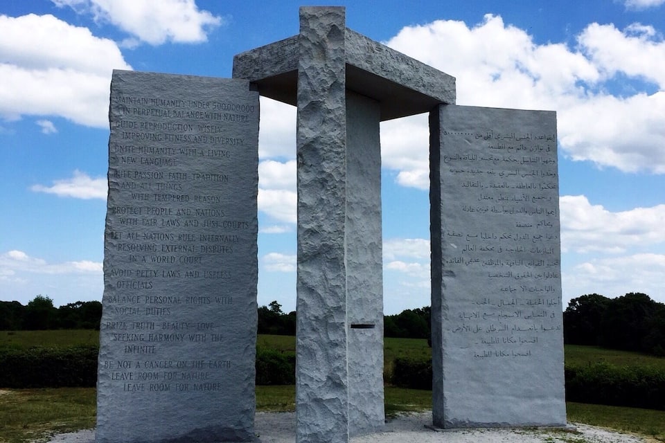 A stone monument with inscriptions in Arabic, set against a clear blue sky with scattered clouds.