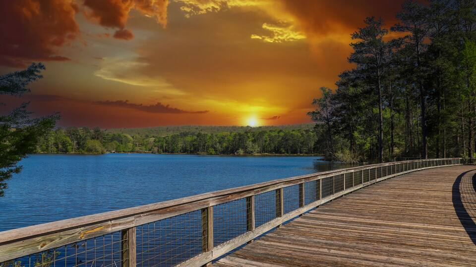 A wooden boardwalk by a lake with a sunset in the background.