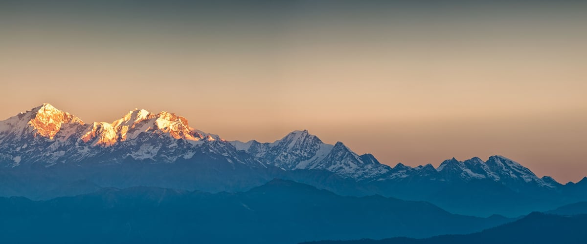 A mountain range with snow-capped peaks and a sunset sky.