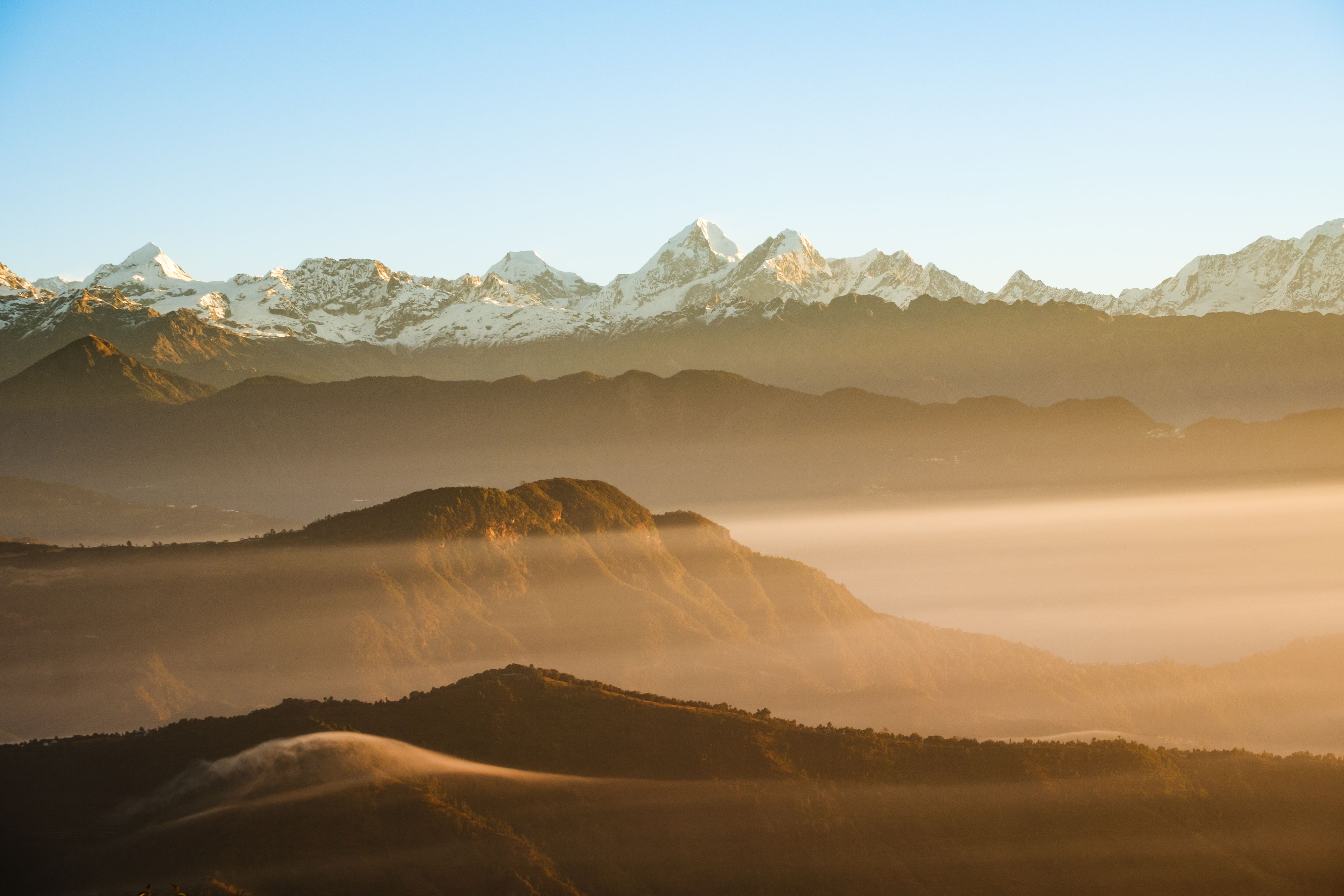 Une chaîne de montagnes aux sommets enneigés et une vallée aux collines enveloppées de brume.