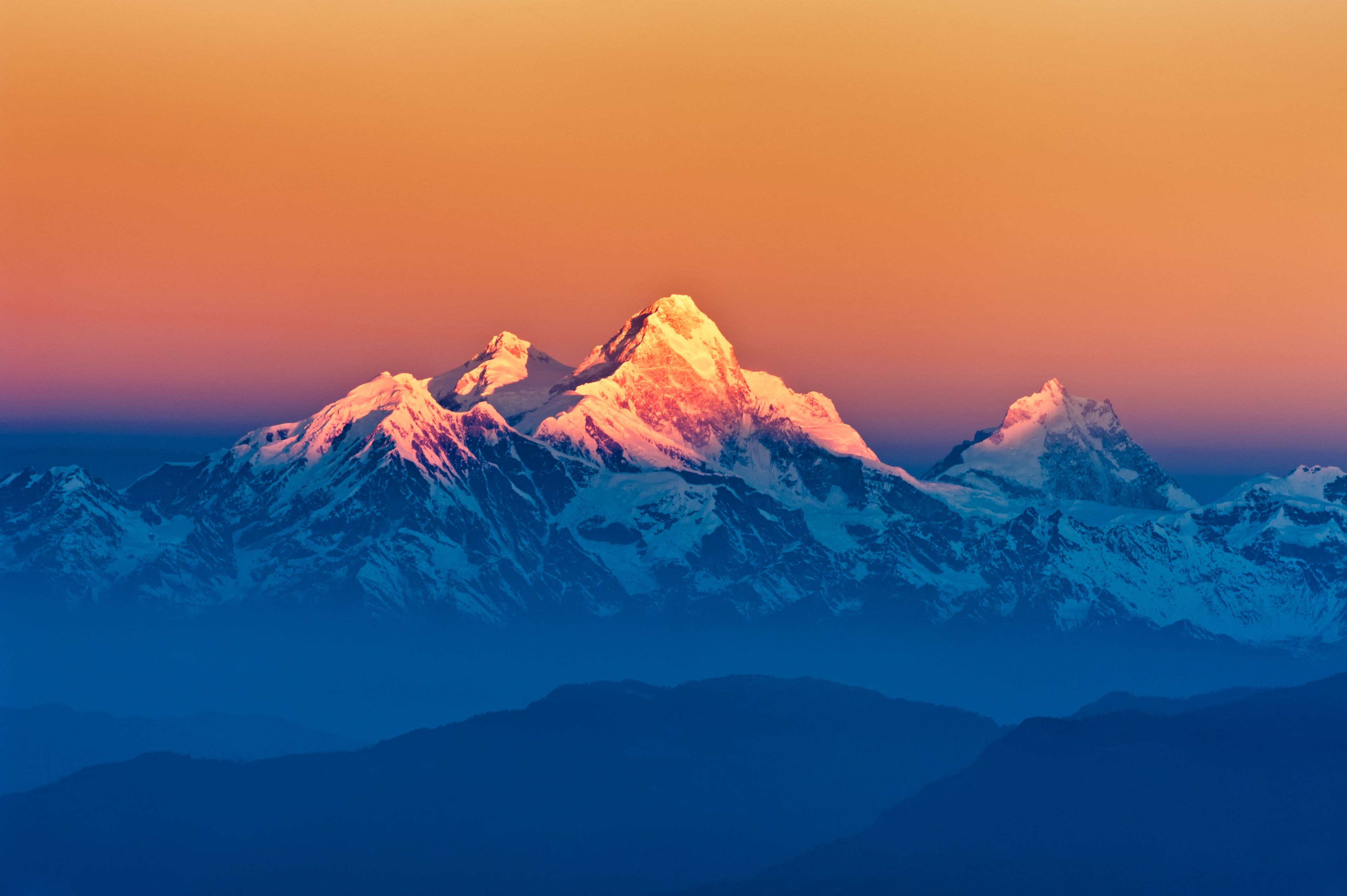 Une chaîne de montagnes dont les sommets enneigés sont illuminés par le soleil couchant.