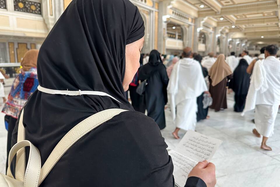 A person in black attire holding a book in a spacious, ornate hall with high ceilings and marble floors.