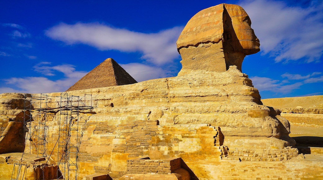 A grand view of the Great Sphinx of Giza with scaffolding for restoration work on a bright hot day on the Giza plateau with the Pyramid of Khufu in the background