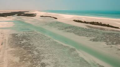 A coastal landscape with clear turquoise waters, sandy beaches, and scattered vegetation.