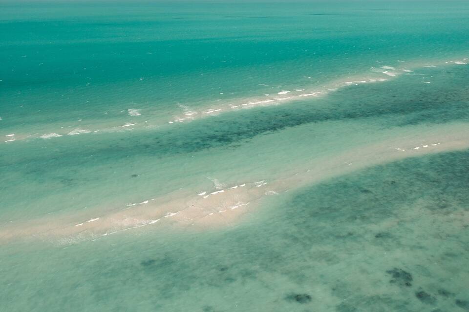 A clear aerial view of a beach with visible sand and shallow water.