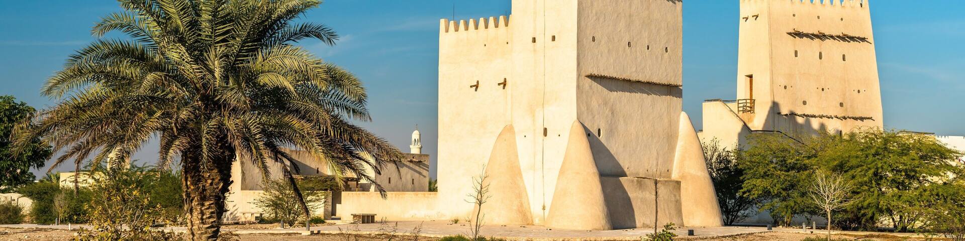 A historic fort with two prominent towers, palm trees, and a clear blue sky.