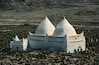 A white building with two conical roofs and a smaller structure with a dome, surrounded by a rocky landscape.