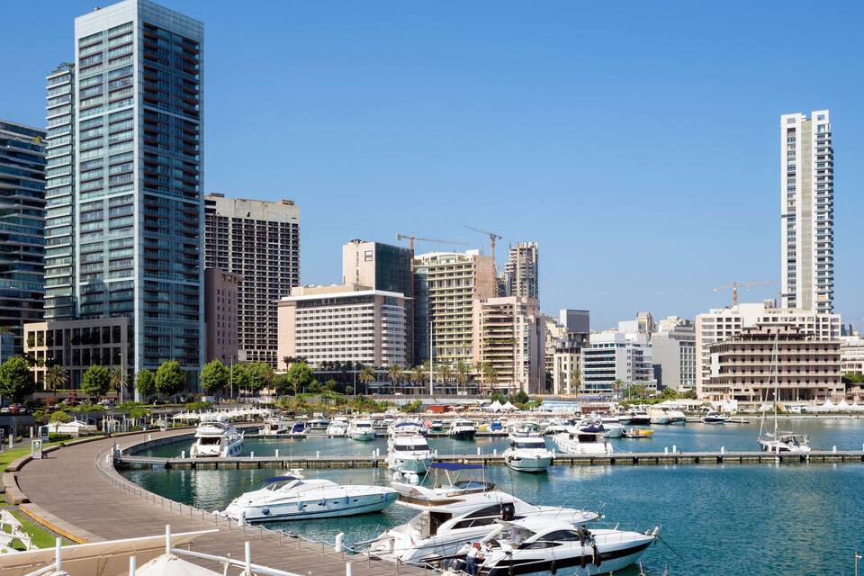 A marina with boats docked, surrounded by high-rise buildings and a clear blue sky.