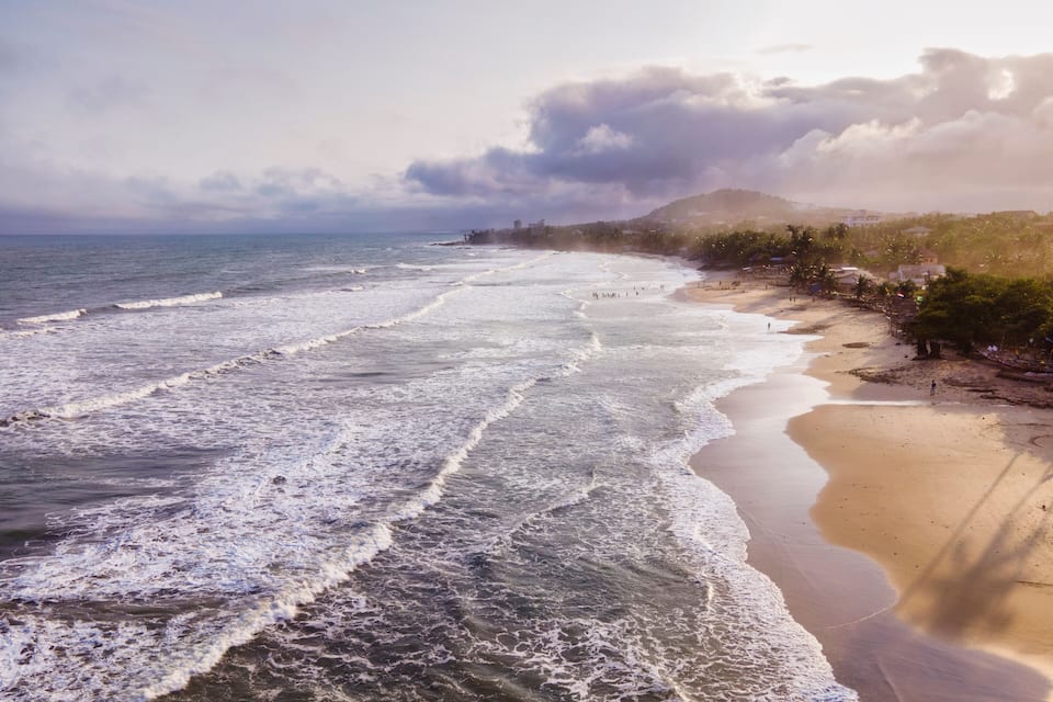 A beach with waves, a sandy shore, and a distant mountain.