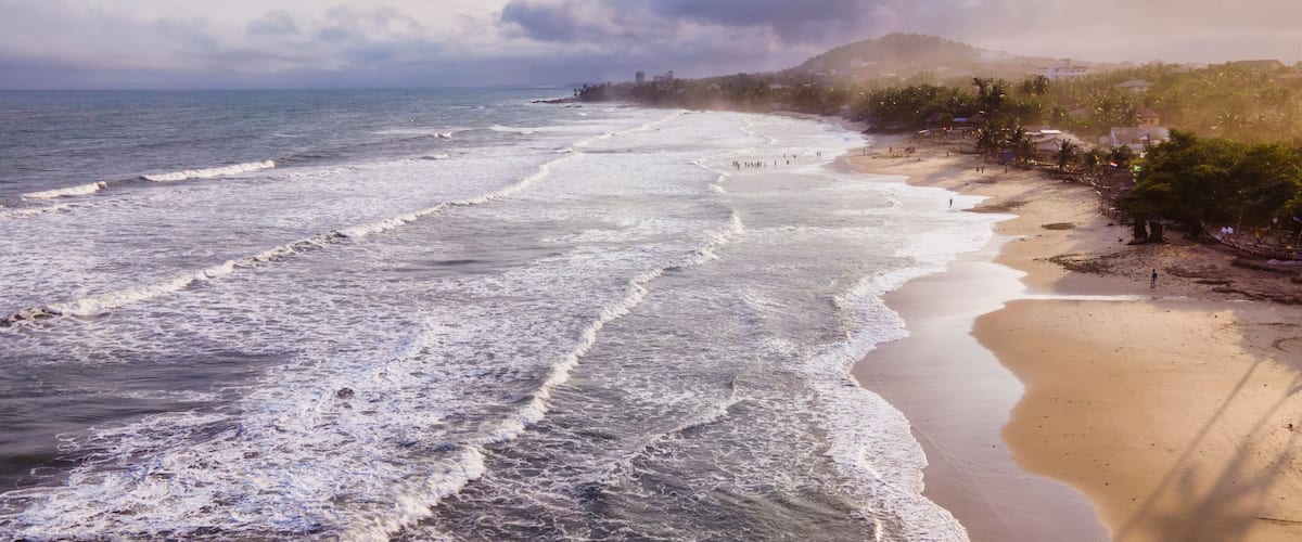 A beach with waves, a sandy shore, and a distant mountain.