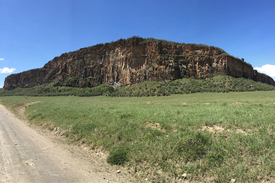Uma estrada de terra que leva a uma grande colina rochosa com vegetação escassa.