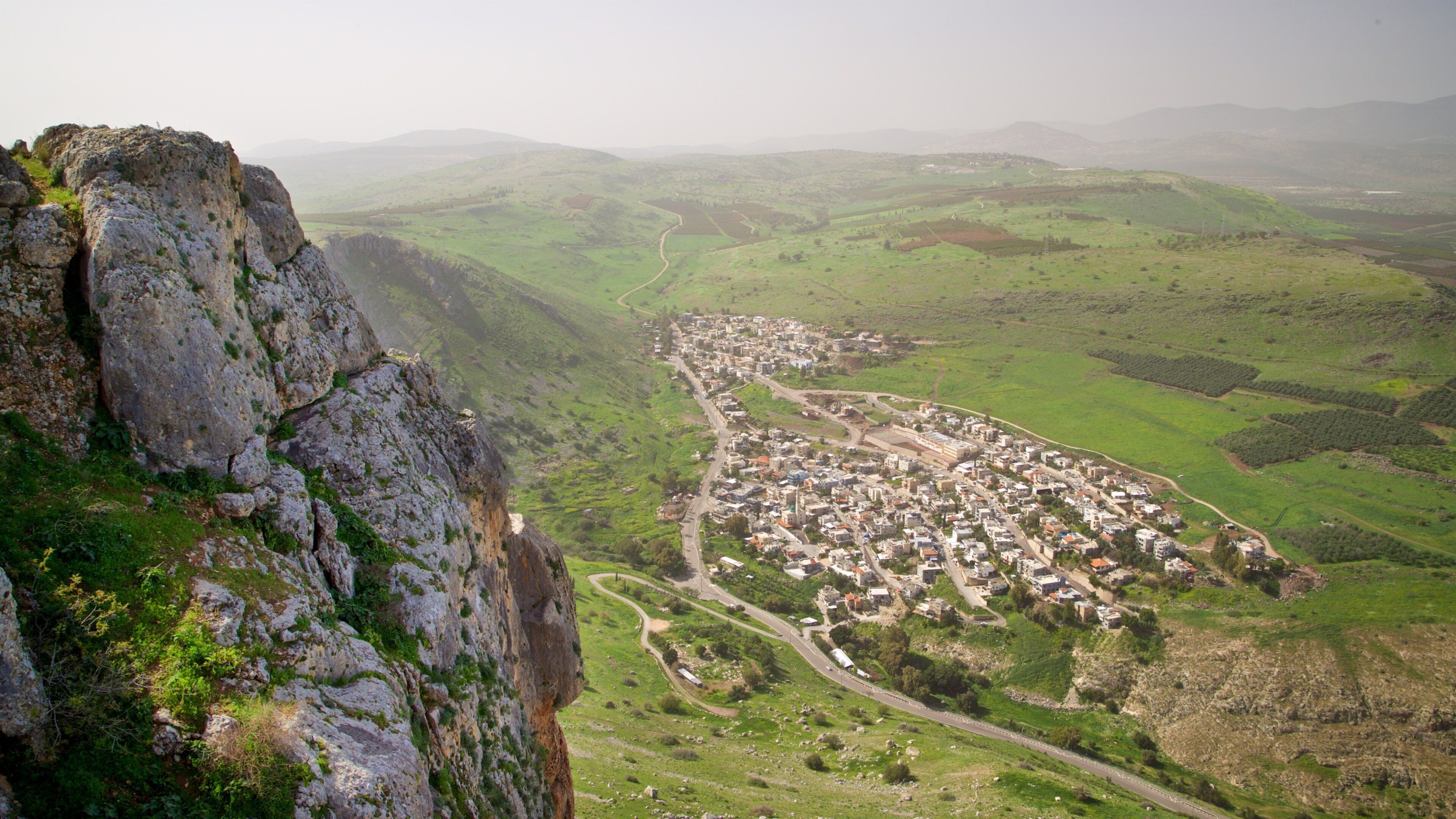 A town nestled in a valley with a prominent rocky cliff on the left.