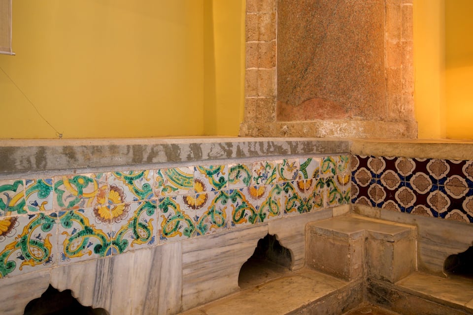 A tiled bench with colorful patterns, a stone wall, and a yellow wall.