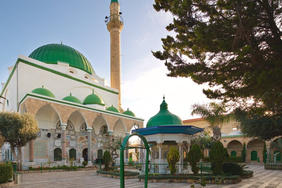A mosque with a tall minaret and green domes.