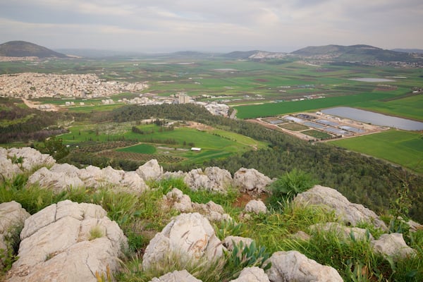 Un paysage montagneux comprenant une ville, des champs verdoyants et une vaste zone industrielle.