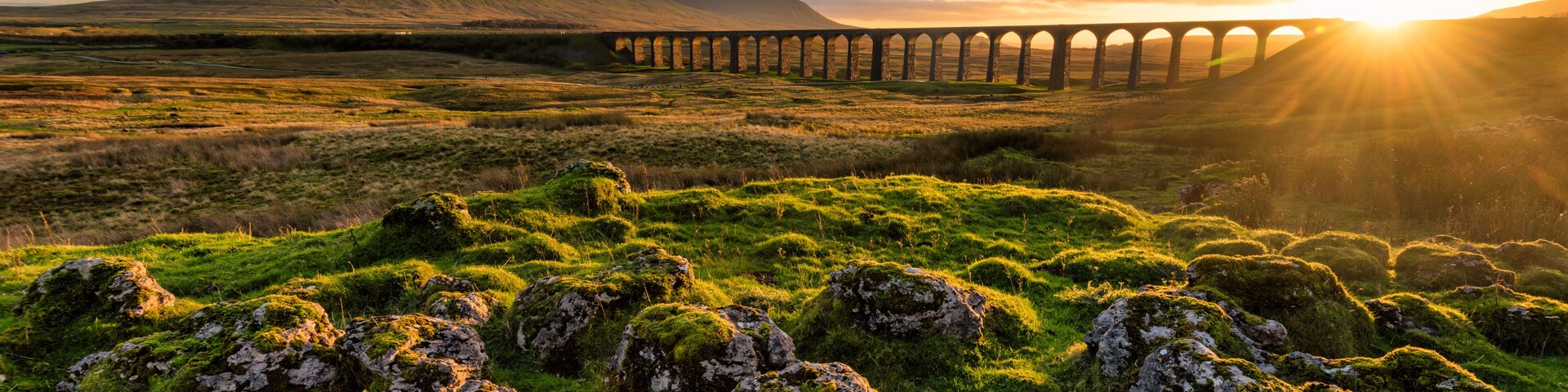 Gorgeous golden light as the sun sets behind the Ribblehead Viaduct with rocks in foreground.